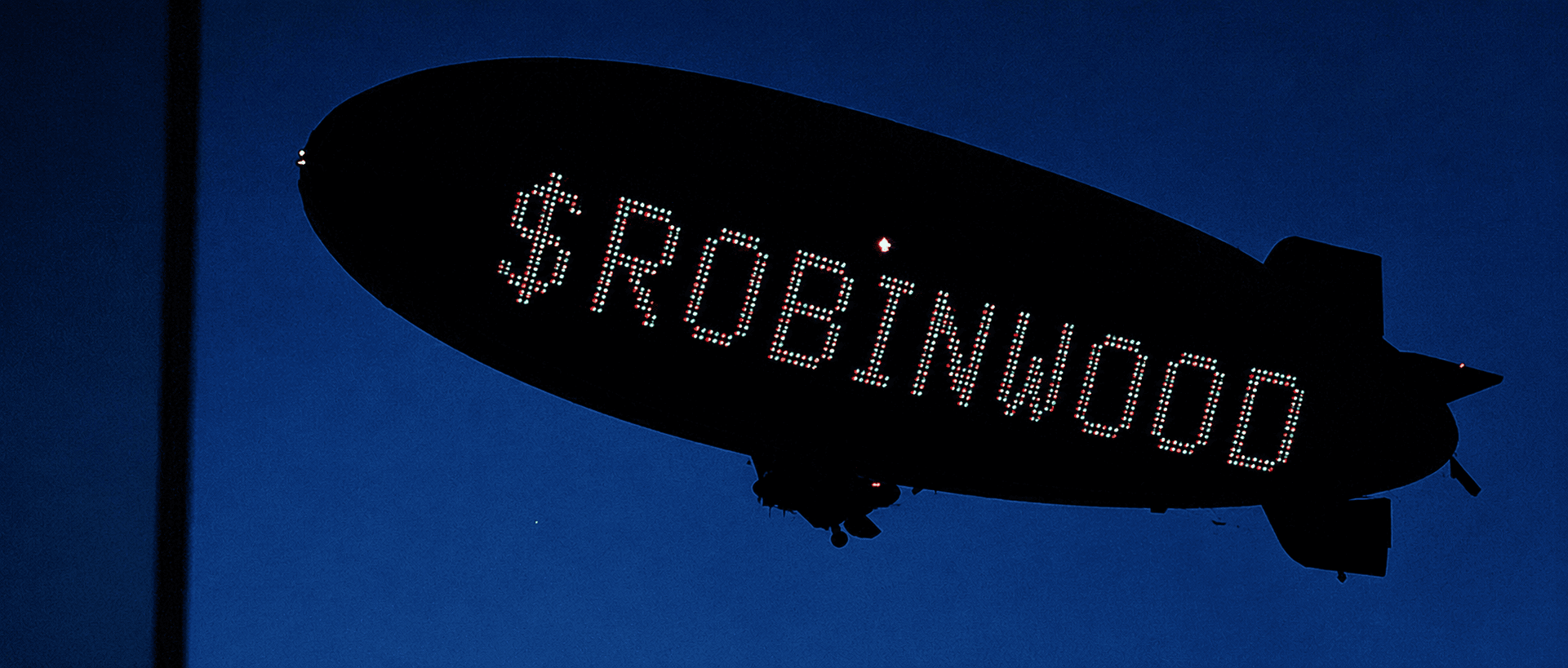 A blimp carrying the illuminated $ROBINWOOD name across the night sky